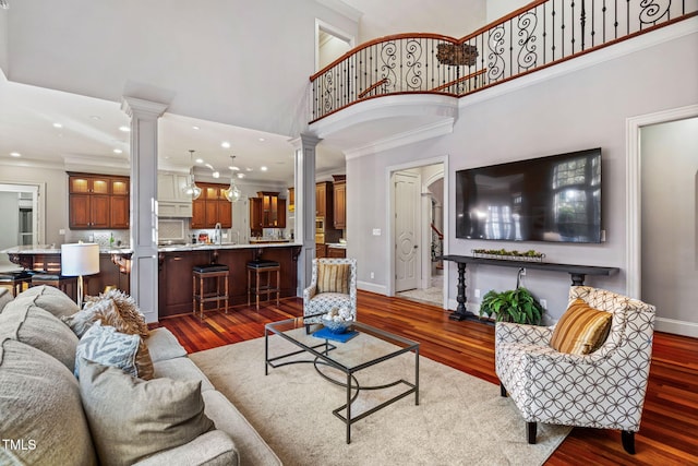 living room with dark hardwood / wood-style flooring, crown molding, decorative columns, and a high ceiling