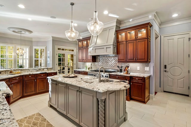 kitchen with backsplash, light stone counters, an island with sink, decorative light fixtures, and french doors