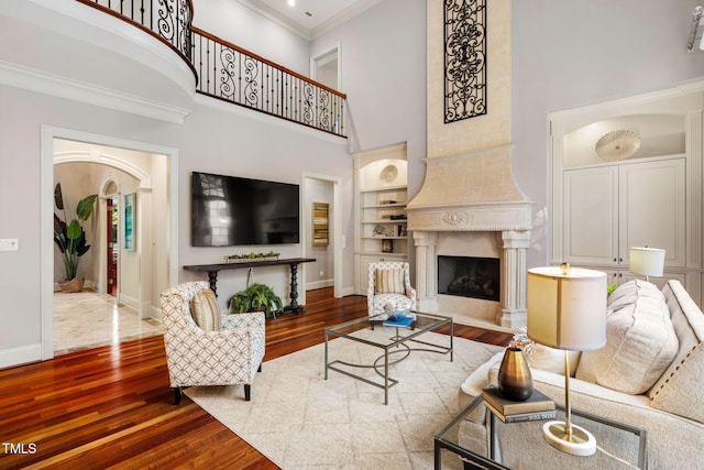 living room featuring a premium fireplace, built in shelves, hardwood / wood-style flooring, and a high ceiling