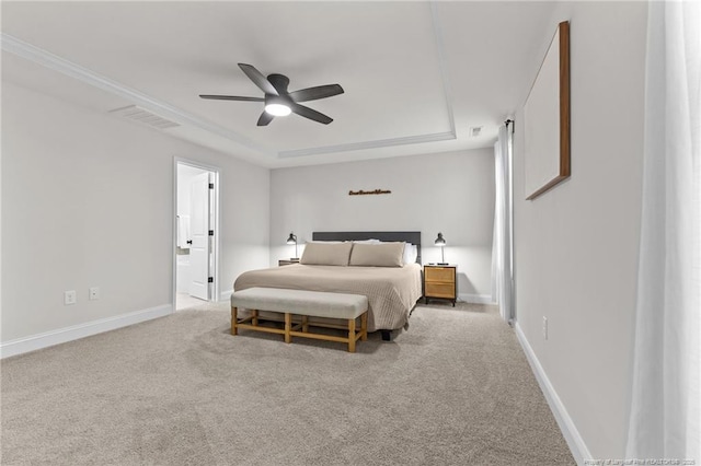 bedroom with a tray ceiling, ensuite bath, light colored carpet, and ceiling fan