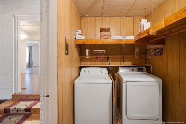 laundry area with washer and clothes dryer, wooden walls, and brick wall