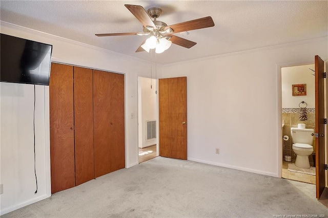 unfurnished bedroom featuring light carpet, ensuite bath, a closet, and ceiling fan