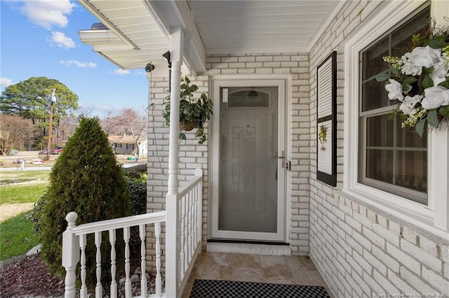 doorway to property with stone siding, covered porch, and brick siding