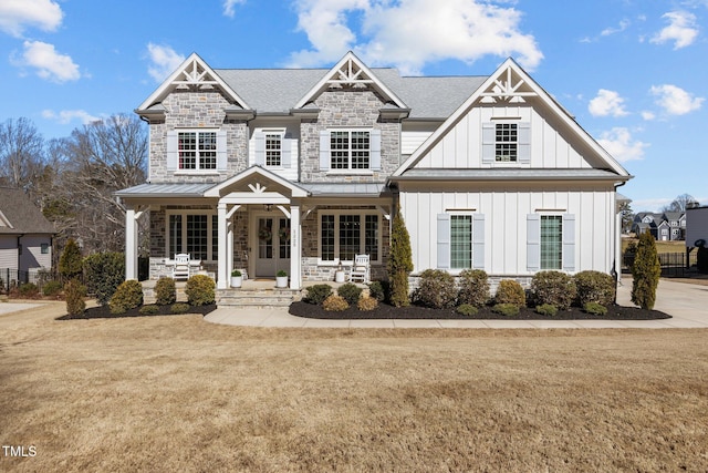 view of front of home with board and batten siding, a front yard, stone siding, and covered porch