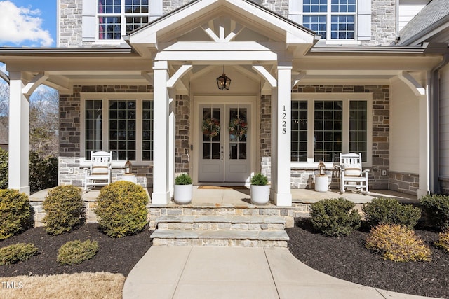 view of exterior entry featuring stone siding, covered porch, and french doors