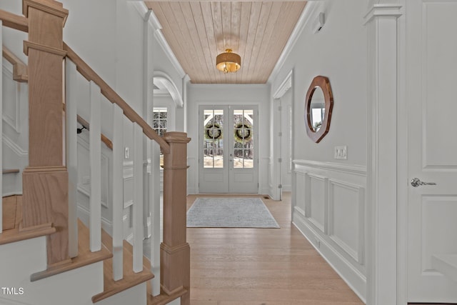 foyer with french doors, a decorative wall, light wood-style flooring, ornamental molding, and wooden ceiling