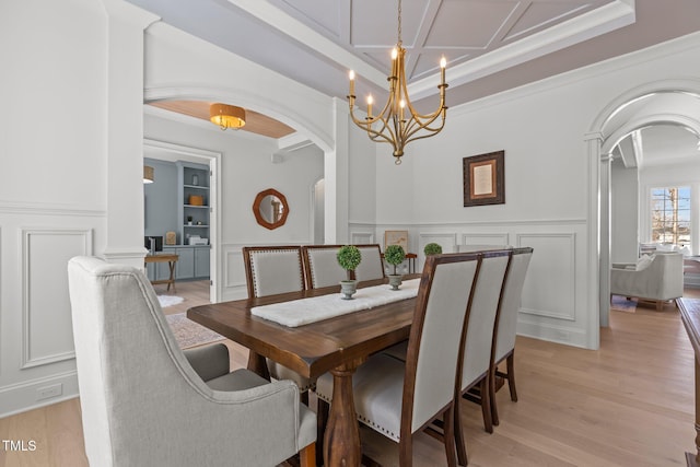 dining area with arched walkways, a notable chandelier, a decorative wall, and light wood finished floors