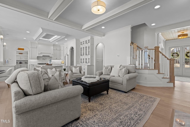 living area featuring arched walkways, light wood-style flooring, stairs, french doors, and beamed ceiling