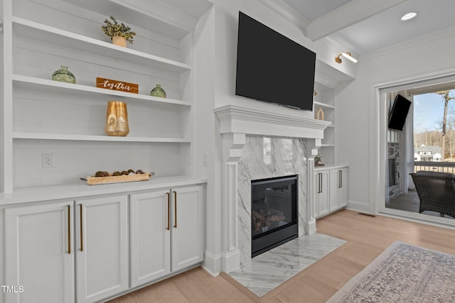 living area with built in shelves, light wood-type flooring, visible vents, and a high end fireplace