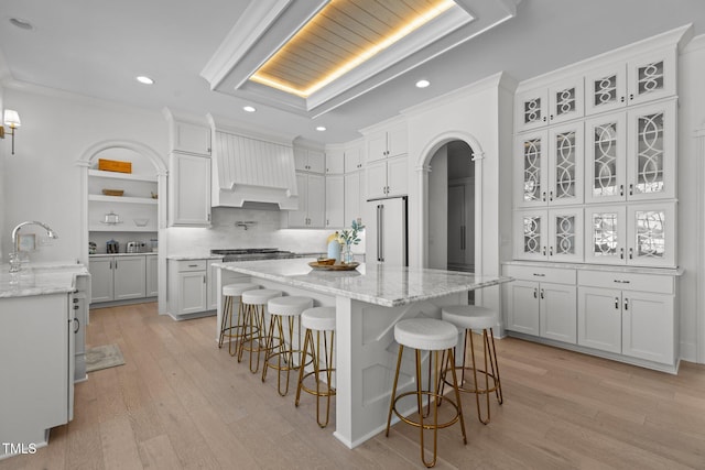 kitchen featuring arched walkways, high quality fridge, a breakfast bar, custom exhaust hood, and light wood finished floors