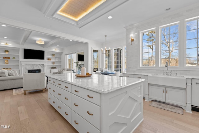 kitchen featuring light wood-type flooring, a kitchen island, a fireplace, and a sink