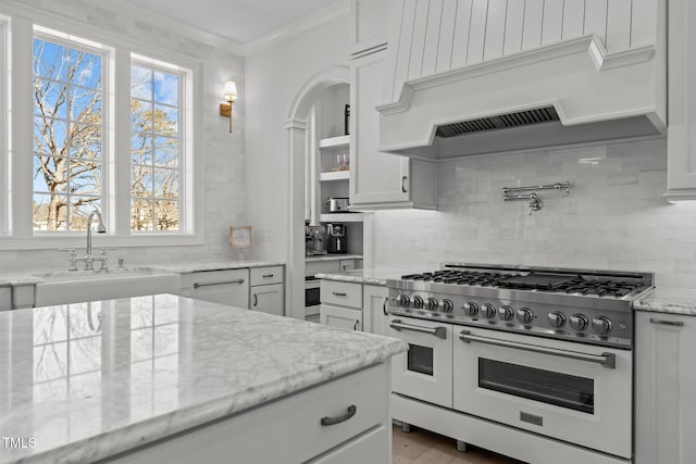 kitchen with light stone counters, decorative backsplash, white cabinets, a sink, and double oven range