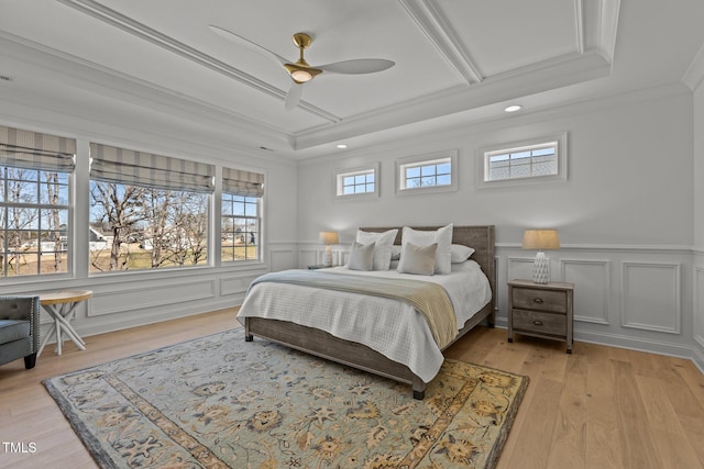 bedroom with a decorative wall, ornamental molding, a ceiling fan, wainscoting, and light wood-type flooring