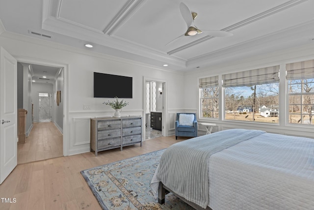 bedroom with wainscoting, light wood-type flooring, visible vents, and crown molding