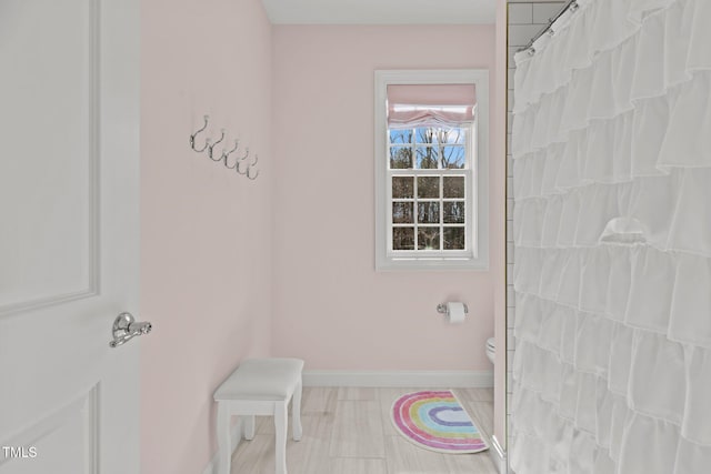 full bath featuring toilet, baseboards, and a shower with shower curtain