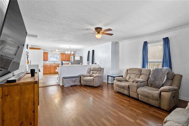 living room with ceiling fan with notable chandelier, ornamental molding, light hardwood / wood-style floors, and a textured ceiling