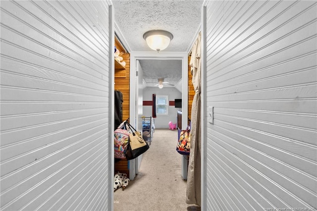 hallway with light carpet, a textured ceiling, and wood walls