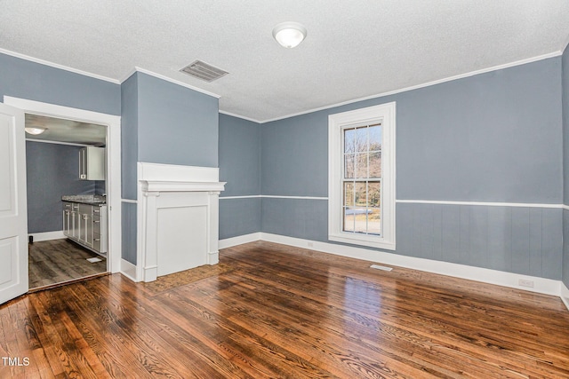 spare room featuring a textured ceiling, a wainscoted wall, dark wood-style flooring, visible vents, and crown molding