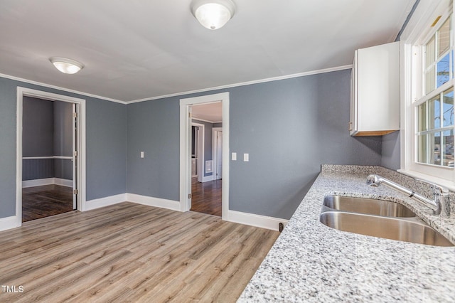 kitchen featuring a sink, light wood-style floors, baseboards, ornamental molding, and light stone countertops