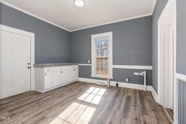 unfurnished dining area with wainscoting, wood finished floors, visible vents, and crown molding