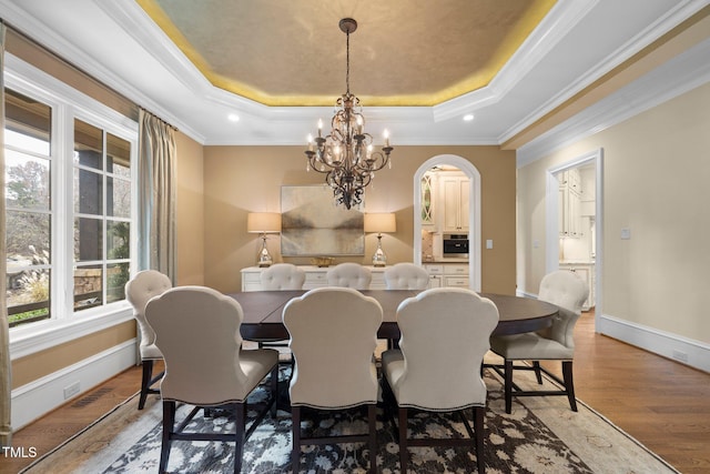 dining space featuring a tray ceiling, ornamental molding, light hardwood / wood-style floors, and a chandelier