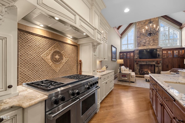 kitchen featuring a fireplace, lofted ceiling, double oven range, light stone counters, and custom range hood