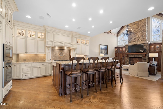 kitchen featuring appliances with stainless steel finishes, tasteful backsplash, a kitchen island with sink, light stone counters, and cream cabinets