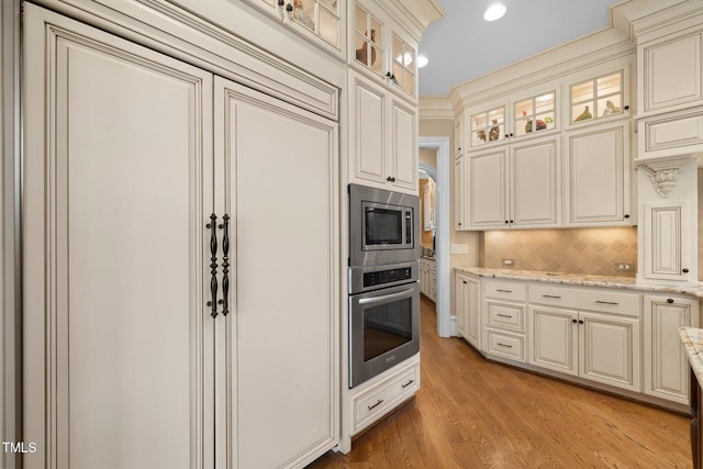 kitchen featuring stainless steel appliances, cream cabinets, light stone counters, and decorative backsplash