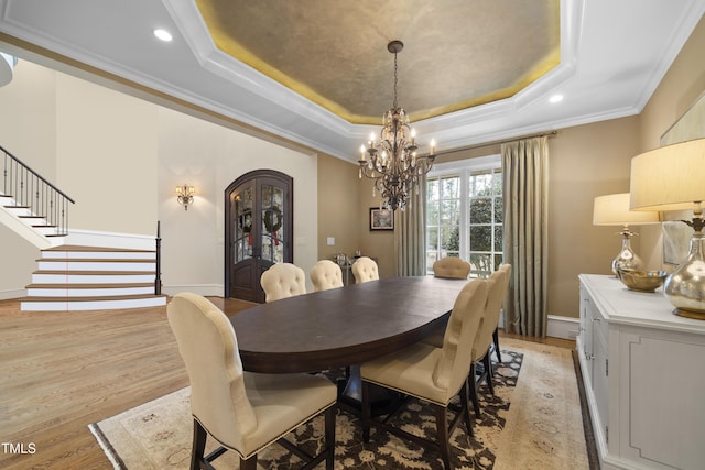 dining area with a raised ceiling, ornamental molding, a chandelier, and light hardwood / wood-style floors