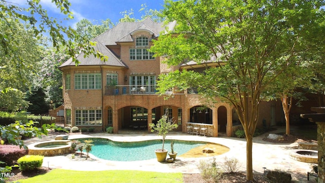 rear view of house with a balcony, a pool with hot tub, and a patio area