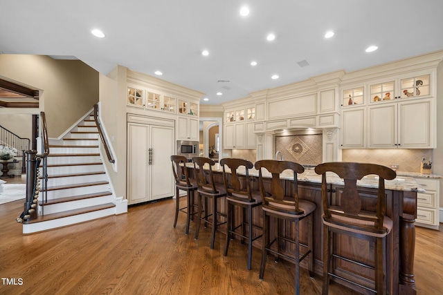 kitchen with hardwood / wood-style floors, built in appliances, cream cabinets, tasteful backsplash, and a center island with sink