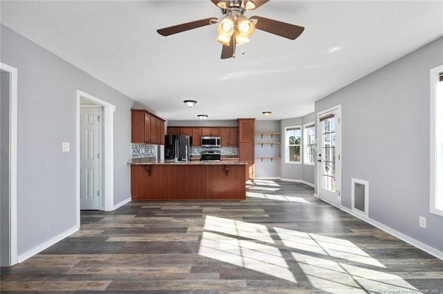 kitchen with dark wood-type flooring, a kitchen breakfast bar, stainless steel appliances, tasteful backsplash, and kitchen peninsula