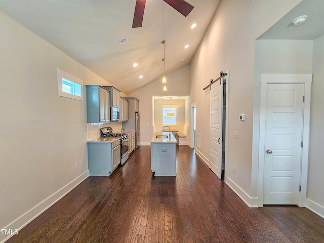 kitchen with appliances with stainless steel finishes, an island with sink, sink, hanging light fixtures, and a barn door