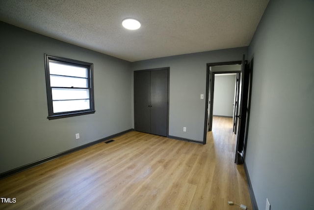 unfurnished bedroom with a textured ceiling, a closet, and light wood-type flooring