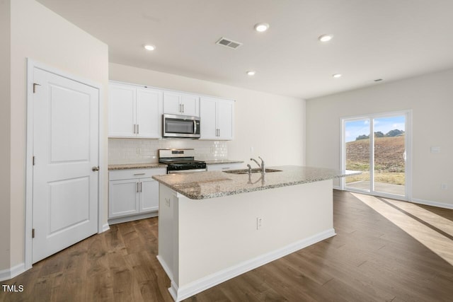 kitchen with appliances with stainless steel finishes, white cabinetry, an island with sink, sink, and dark hardwood / wood-style flooring