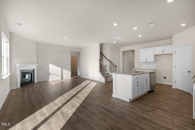 kitchen with tasteful backsplash, light stone counters, dishwasher, a kitchen island with sink, and white cabinets