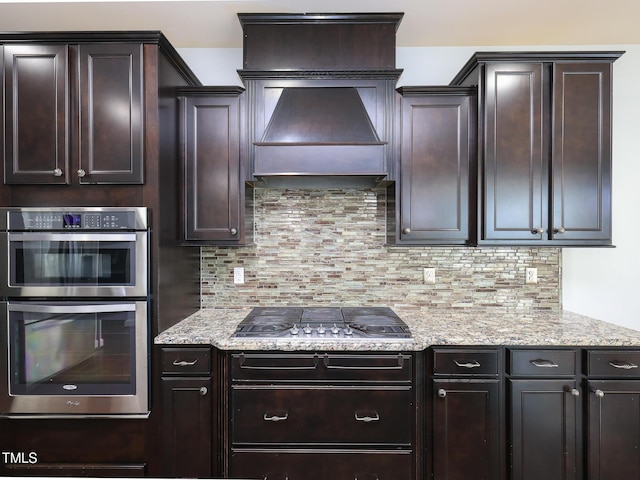 kitchen with tasteful backsplash, light stone countertops, appliances with stainless steel finishes, and dark brown cabinets