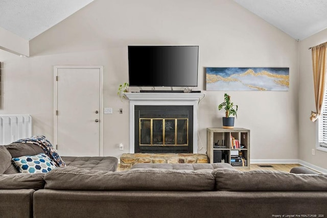 living room featuring hardwood / wood-style flooring, vaulted ceiling, and a stone fireplace