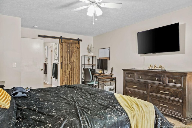 bedroom with ceiling fan, a barn door, and a textured ceiling