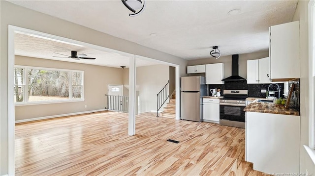 kitchen featuring wall chimney exhaust hood, appliances with stainless steel finishes, light hardwood / wood-style floors, decorative backsplash, and white cabinets