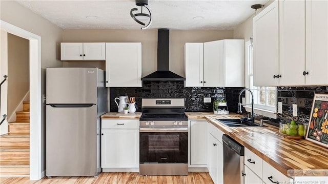 kitchen featuring sink, wooden counters, appliances with stainless steel finishes, wall chimney range hood, and white cabinets