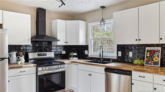 kitchen featuring wood counters, wall chimney exhaust hood, sink, white cabinetry, and stainless steel appliances