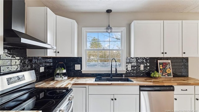 kitchen with wall chimney range hood, sink, appliances with stainless steel finishes, white cabinets, and decorative light fixtures