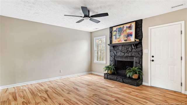 unfurnished living room featuring hardwood / wood-style flooring, ceiling fan, a stone fireplace, and a textured ceiling