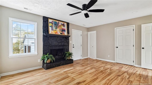 unfurnished living room with ceiling fan, a fireplace, a textured ceiling, and light wood-type flooring