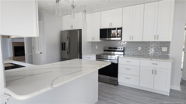 kitchen featuring appliances with stainless steel finishes, white cabinets, hanging light fixtures, light stone counters, and light hardwood / wood-style floors