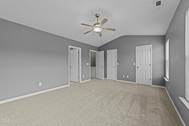 unfurnished bedroom with light carpet, ceiling fan, vaulted ceiling, and multiple closets