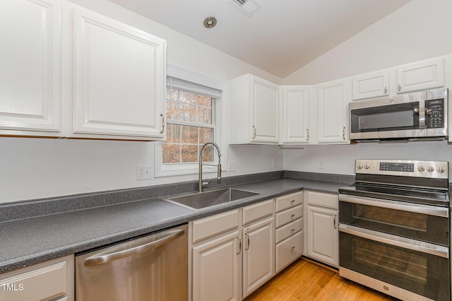 kitchen featuring stainless steel appliances, dark countertops, a sink, and white cabinetry