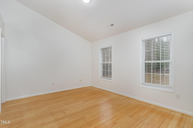 spare room featuring lofted ceiling, light wood-style flooring, visible vents, and baseboards