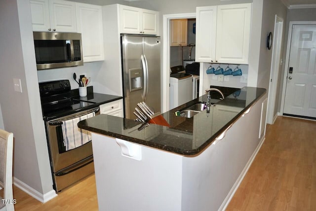 kitchen with washer and clothes dryer, appliances with stainless steel finishes, white cabinetry, dark stone countertops, and light wood-type flooring